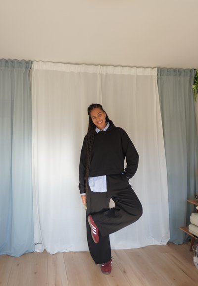 Sudadera recortada negra, camisa de color azul claro con cuello debajo, pantalones anchos negros y zapatillas rojas sobre un fondo claro.