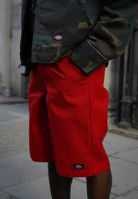 Rode shorts gemaakt van duurzaam materiaal, met een rechte snit en een merkembleem. Gecombineerd met een camouflagejas, die contrasterende kleuren laat zien.