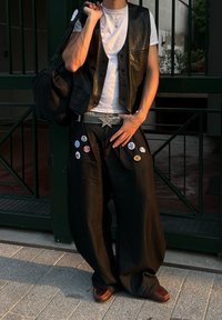 Veste en cuir noir portée sur un T-shirt blanc, associée à un pantalon large noir orné de divers boutons et d'une boucle de ceinture en forme d'étoile argentée. Chaussures marron.