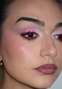 Lähikuva kasvoista, joissa on vaaleanpunaista luomiväriä, tummaa eyelineria ja runsaita ripsiä. Kiiltävät murrettu vaaleanpunaiset huulet ja pehmeä vaaleanpunainen poskipuna sileällä iholla.