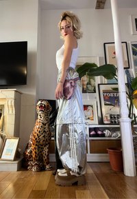Pantalon large en métal argenté avec des rayures blanches, associé à un débardeur blanc ajusté et des bottines à plateforme marron épaisses.