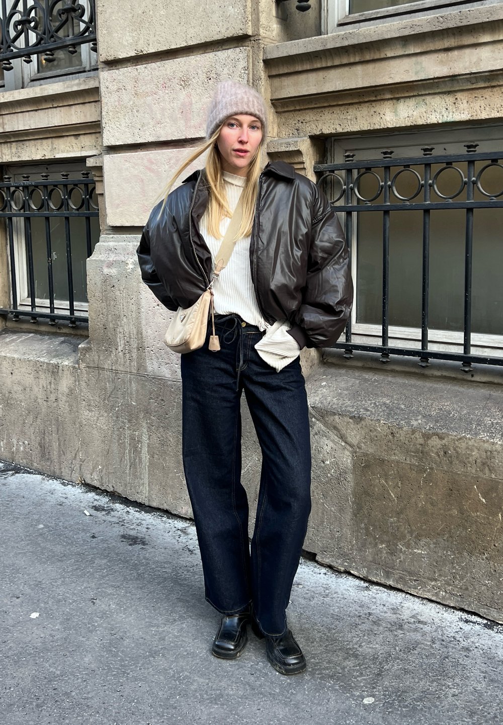Καφέ μποφάν μπουφάν πάνω από ένα λευκό ριγωτό πουλόβερ, σκούρες μπλε φαρδιές τζιν παντελόνες, μαύρες χοντρές μπότες και ένα ανοιχτό ροζ πλεκτό σκουφάκι.