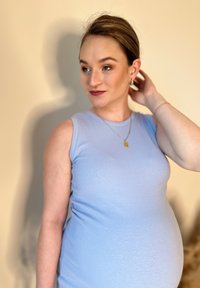 Top in cotone azzurro chiaro a costine con una vestibilità aderente, indossato da una persona con una pancia visibile. Collana con catena e pendente rettangolare.