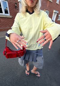 Sárga bordázott hosszúujjú felső tengerészkék gallérral, szürke redős szoknya, piros mini táska és színes körmök. A megjelenést flip-flop papucsok egészítik ki.