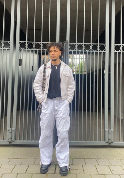 Chaqueta de denim blanca sobre una camiseta negra, combinada con pantalones cargo blancos y botas negras. Bolso de hombro texturizado con un patrón de cuadros.