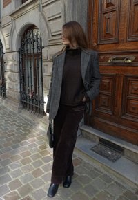 Grå rutete blazer, brun strikket genser, brune kordfløyelsbukser, svarte ankelstøvler og en svart veske foran en tredør og brosteinsbelagt fortau.