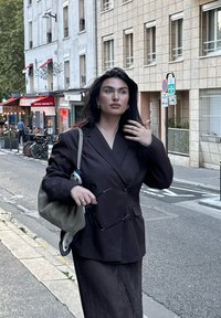 Tamno preveliko sako s dvostrukim kopčanjem, uparen s teksturiranom crnom suknjom. Nosila je bež torbu preko ramena i držala sunčane naočale.