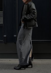 Melnas ādas jaka valkāta virs pelēka maksi svārku ar augstu iedalījumu. Apģērbs saskaņots ar melnām augstpapēžu kurpēm.