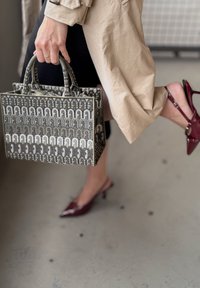 Gemusterte Handtasche in Grau und Weiß mit strukturiertem Design; kombiniert mit glänzenden burgunderfarbenen spitzen Absatzschuhen. Strukturierte Oberfläche sichtbar.