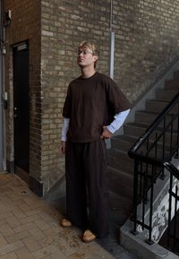 T-shirt oversize en coton brun associé à un pantalon ample assorti, avec un tissu texturé et des manches longues blanches contrastantes. Sabots en bois.