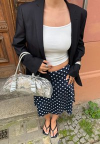 Čierne sako cez biele tielko, skombinované s námornícky sukňou s bodkami. Strieborná taška s flitrami s dvoma rúčkami a plážové sandále.