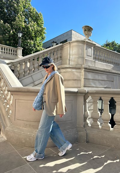 Blazer beige sobre una camisa de color azul claro con cuello, combinado con jeans de pierna ancha. Un bolso acolchado azul claro y zapatillas blancas completan el look.