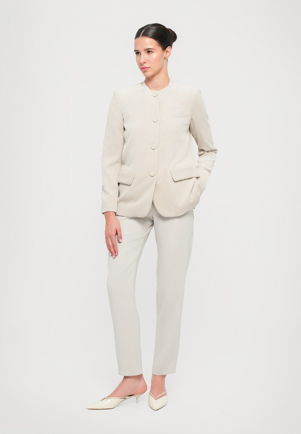 Blazer en velours côtelé beige clair avec un col haut, deux poches avant et fermeture à boutons, associé à un pantalon beige clair ajusté et des ballerines pointues.