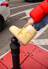 Bota Yellow Moon con superficie texturizada, cuello acolchado y banda con logo blanco, colocada sobre un poste negro contra un fondo de pavimento gris.