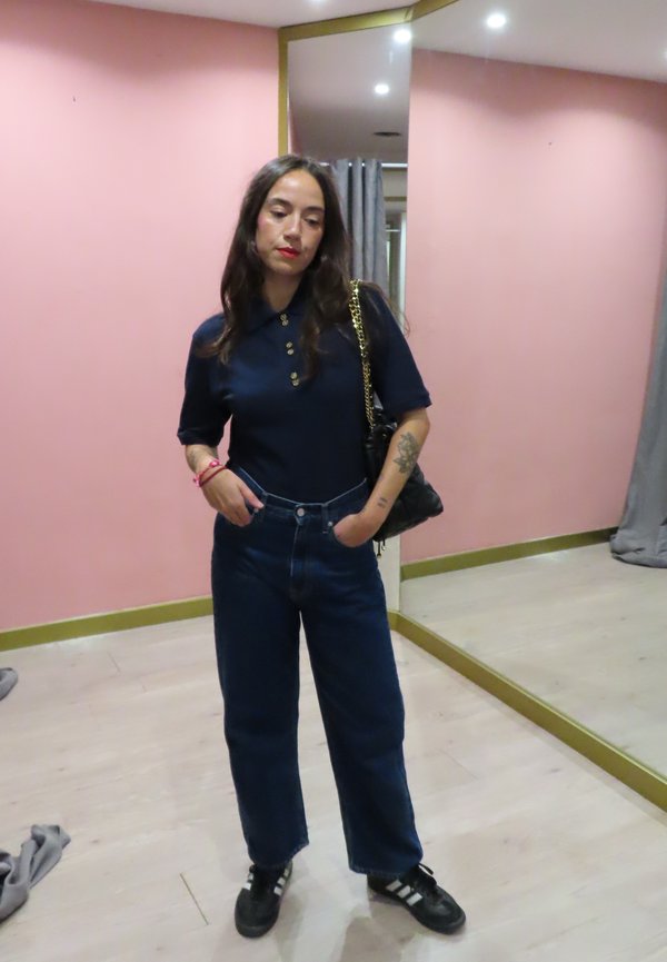 Tumesinine polo särk nööpidega, kõrge talje denim teksad ja must crossbody kott. Mustad tossud valgete triipudega. Peeglid ja roosa taust.
