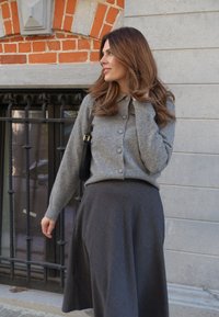 Hellgraue, knöpfbare Strickjacke aus weichem Strick, kombiniert mit einem dunkelgrauen ausgestellten Rock. Das Outfit verfügt über einen Kragen und eine leicht lockere Passform.
