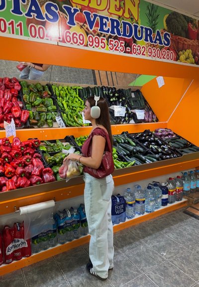Sección de productos frescos en un mercado con pimientos rojos, pimientos verdes y calabacines. Estantes naranjas con recipientes de plástico transparente.