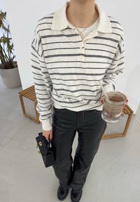 Chemise à manches longues blanche à rayures avec un col chemise, associée à un pantalon en cuir noir. Tient un bocal en verre et un petit sac à main noir.