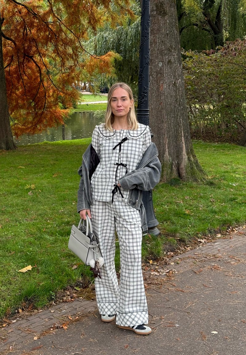 Tenue à carreaux en blanc et noir avec un col à volants, veste marron et sac à main gris. Pantalon à jambes larges, accessoires minimalistes, texture douce.