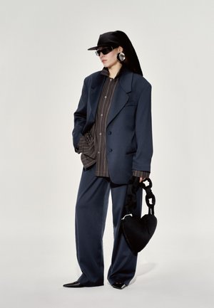 Sacou supradimensionat bleumarin, cămașă cu dungi, pantaloni cu picioare largi, accesorii negre inclusiv o geantă în formă de inimă și ochelari eleganți, pantofi plate.