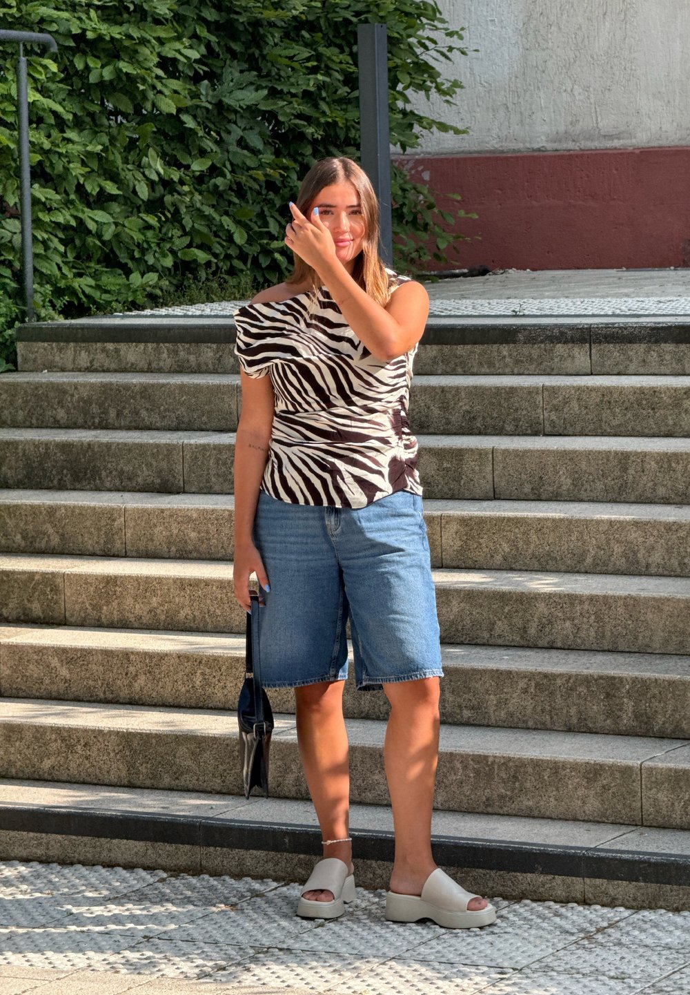 Randig blus i zebramönster med asymmetrisk halsringning, denimbermuda-shorts och beige plattformssandaler. Svart handväska med en smal design.