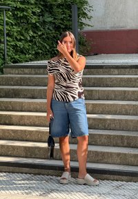 Randig blus i zebramönster med asymmetrisk halsringning, denimbermuda-shorts och beige plattformssandaler. Svart handväska med en smal design.