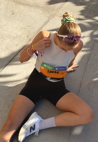 Coureur portant un débardeur blanc et un short noir, avec un chouchou, des lunettes de soleil et des chaussures New Balance. Numéro de dossard 34644 visible.