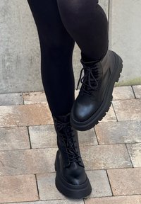 Črni vojaški čevlji z gladkim usnjenim zaključkom, z robustnimi vezalkami, debelim podplatom in visokim dizajnom z teksturirano površino.