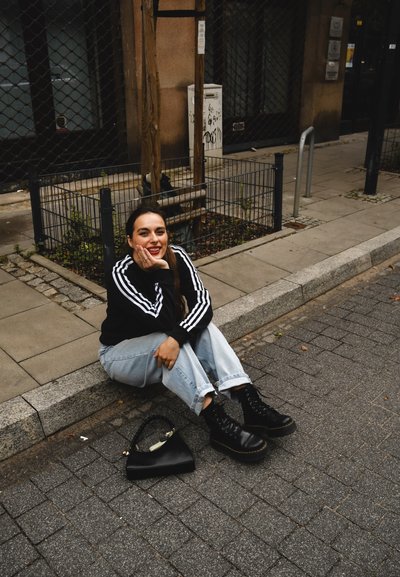 Sudadera negra con rayas blancas, jeans cortos de mezclilla azul claro, botas negras de plataforma y un bolso negro sobre una calle pavimentada.