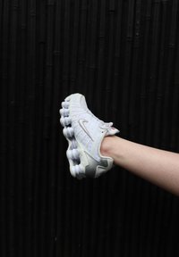 Hvit og sølv atletisk sko med mesh-overdel, teksturerte detaljer og karakteristisk polstret såle. Viser Nike-logoen på siden.