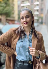 Καφέ σουέντ σακάκι πάνω από τζιν πουκάμισο, μαύρες δερμάτινες παντελόνες, ζώνη με χρυσές λεπτομέρειες, με καλοσχηματισμένη τσάντα χεριού και στρωματωμένα κοσμήματα.