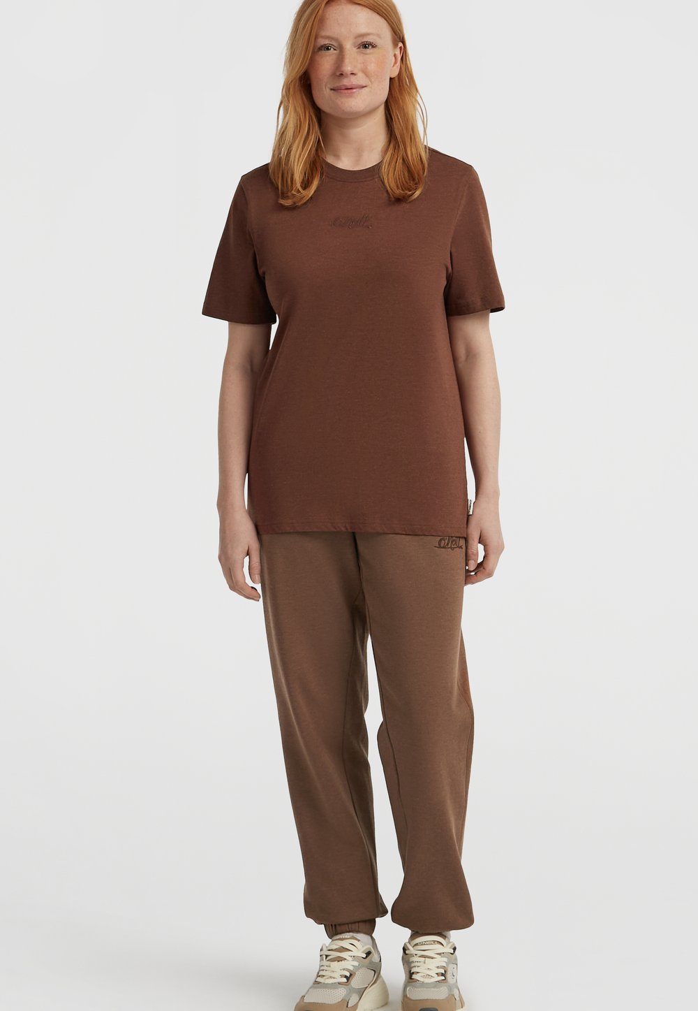 Brązowa bawełniana koszulka z krótkim rękawem, z delikatnym logo. W połączeniu z brązowymi spodniami dresowymi, obie części mają luźny krój i gładką teksturę.