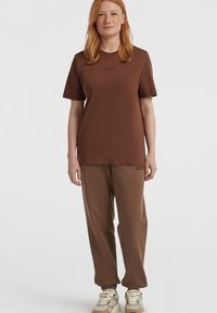 Brązowa bawełniana koszulka z krótkim rękawem, z delikatnym logo. W połączeniu z brązowymi spodniami dresowymi, obie części mają luźny krój i gładką teksturę.