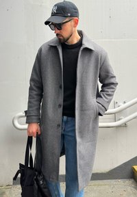 Manteau en laine gris avec un col à revers et cinq boutons, porté sur un pull noir. Associé à un jean bleu et un sac à bandoulière noir.