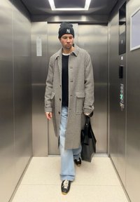 Rutete lang frakk, svart t-skjorte, vide lyseblå jeans, svarte joggesko med brune aksenter, og svart tote bag i en metallisk heis.