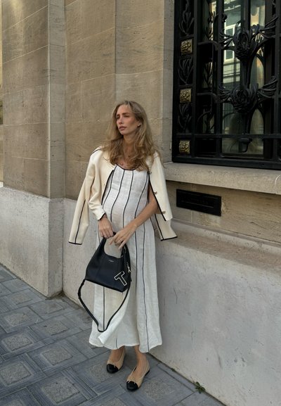 Vestido blanco con líneas verticales azul marino, chaqueta color crema, bolso negro con acentos blancos y bailarinas beige con puntas negras. Texturas suaves.