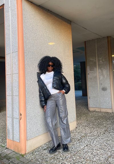 Chaqueta de plumas negra, camisa blanca, pantalones cargo grises con bolsillos y botas negras. Superficies texturizadas y elementos de diseño estructurados.