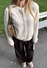 Crème cardigan met knopen, gecombineerd met donkerbruine wijde broek. Beige tas met ritsdetails en lichtbruine instappers.