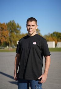 Sort kortærmet t-shirt med en firkantet logo-patch på venstre bryst, lavet af bomuld, med en afslappet pasform og glat tekstur.