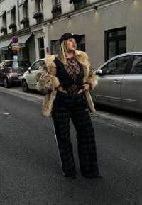 Umelý kožuch na čiernom čipkovanom topi, skombinovaný s plaid širokými nohavicami. Doplnky obsahujú vrstvené náhrdelníky a čiernu čiapku.