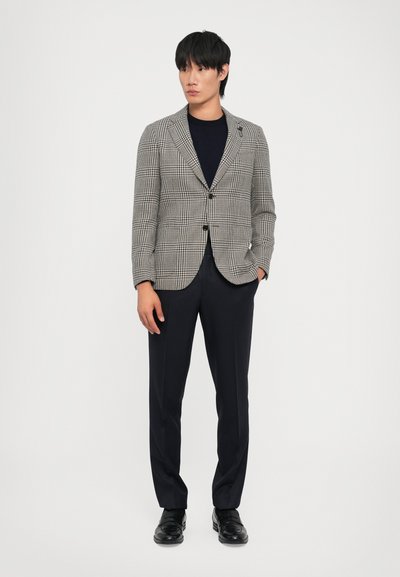 Blazer a cuadros negro y gris con cierre de botón único, combinado con pantalones oscuros y zapatos negros. Tela suave y ajuste a medida.