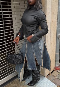 Čierna priliehavá bunda s vysokým golierom, v kombinácii s rozstrapkanou denimovou sukňou. Doplnky zahŕňajú malú čiernu tašku s nitmi. Čierne čižmy na podpätku.