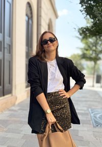 Μαύρο σακάκι, λευκή μπλούζα και μίνι φούστα με λεοπαρτίνα. Καφέ τσάντα, χρυσό ρολόι και γυαλιά ηλίου. Ουρανός της πόλης στο παρασκήνιο.