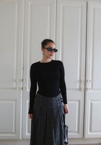 Camisola preta de mangas longas combinada com uma saia xadrez cinza com pregas e detalhes em metal, complementada com óculos de sol escuros e uma bolsa pequena.