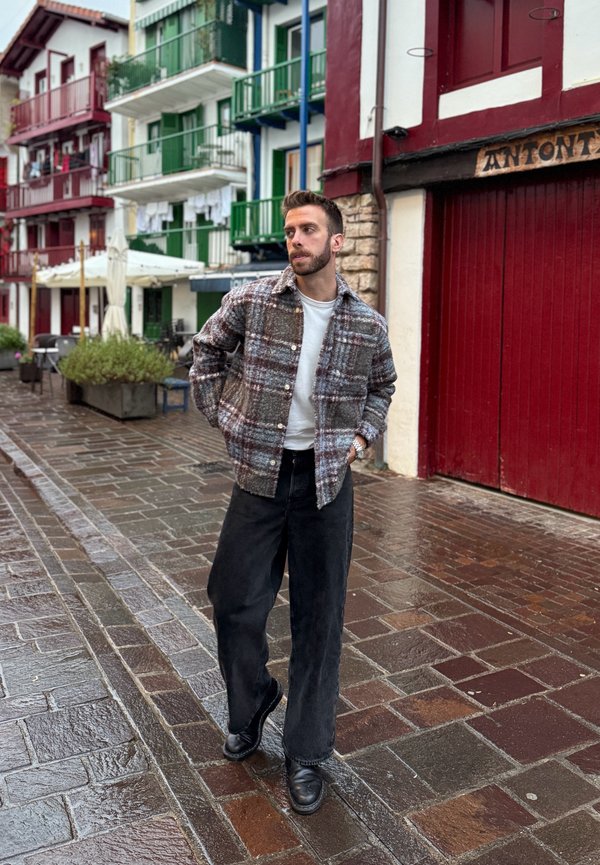 Rutig ulljacka i jordnära toner, kombinerad med en vit skjorta och svarta vida byxor. Svarta läderstövlar fulländar outfiten.