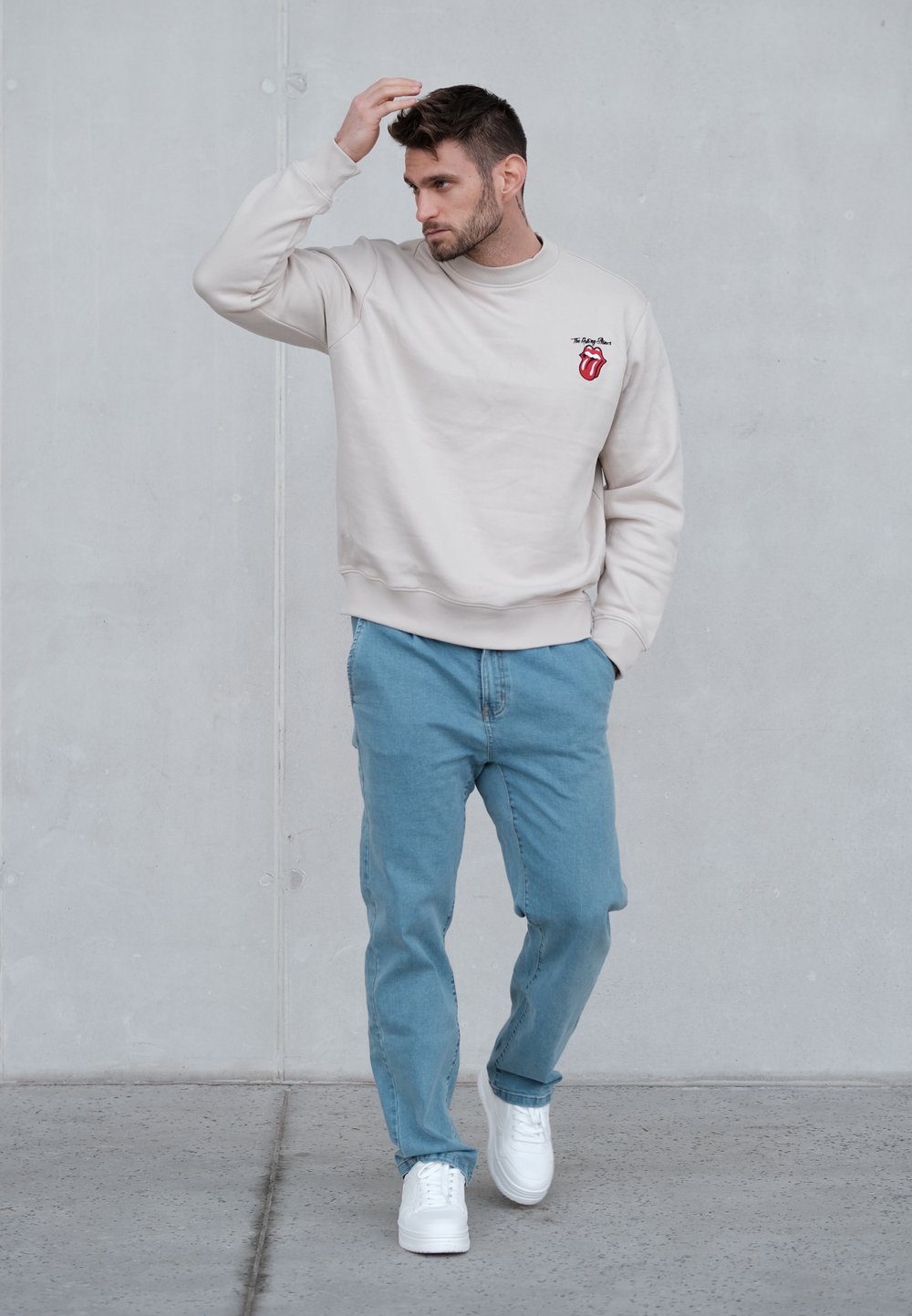 Sudadera beige con el logo de los Rolling Stones, combinada con vaqueros azul claro y zapatillas blancas. Las superficies parecen lisas con un ajuste casual.