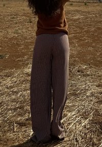 Pantaloni a gamba larga in tessuto a righe marrone e crema, con vita alta e un design fluido, abbinati a un top marrone texturizzato.