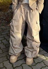 Bēšas kravas bikses no viegla auduma, ar vaļīgu piegriezumu, elastīgu jostasvietu un sānu kabatām. Kombinētas ar biezām bēšām zābakiem.