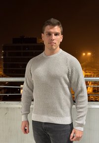 Light grey ribbed jumper with long sleeves and a round neckline, paired with dark jeans. The fabric appears soft with a textured finish.