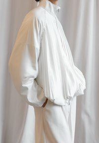 Weiße, gepolsterte Jacke mit plissiertem Design, hohem Kragen und Reißverschluss. Hergestellt aus glattem Material mit gerafften Akzenten am Saum und an den Bündchen.